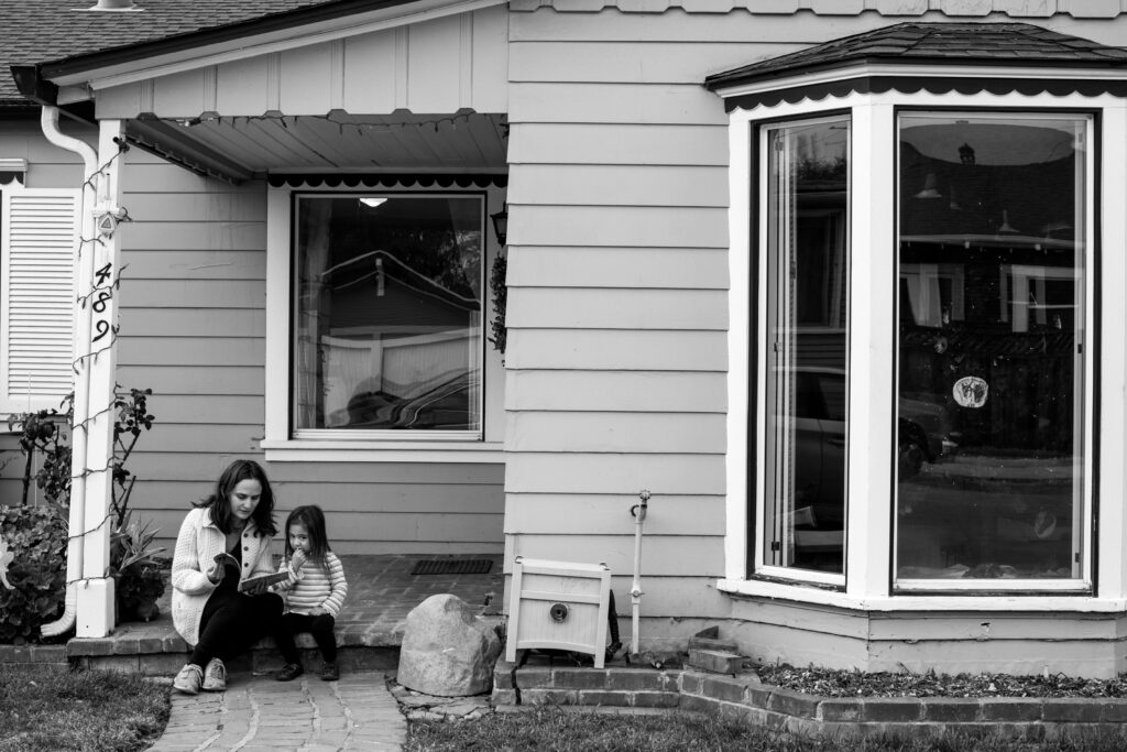 A mom and her daughter sit on their front step reading a book together. 