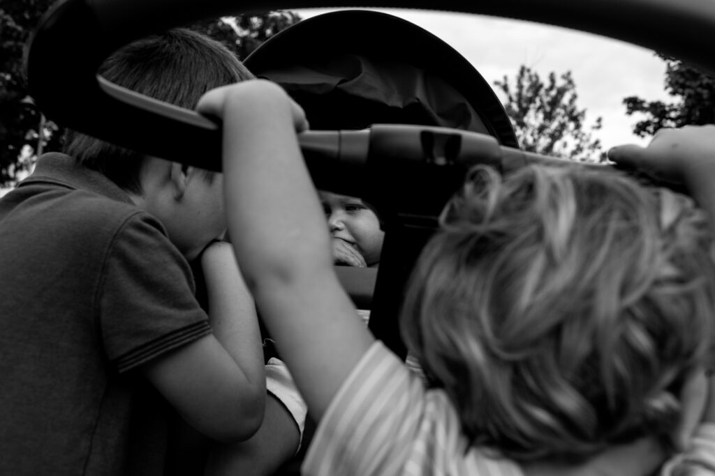 Black and white picture of three small boys hanging onto a stroller with the smallest one sucking his thumb.