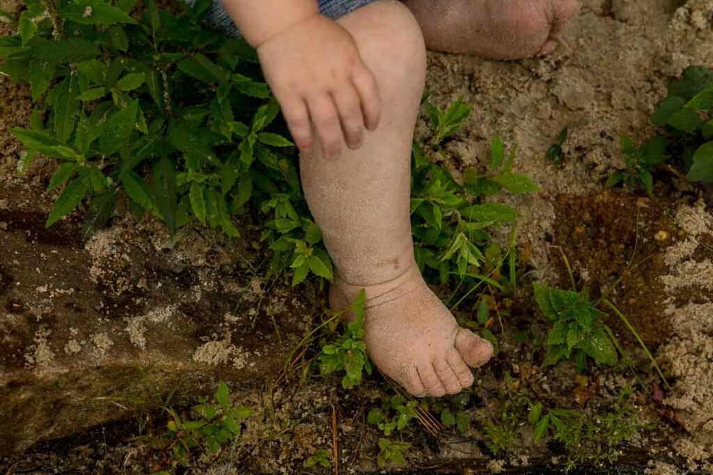 Detail of a toddler's sand covered foot with leaves and sand surrounding him. 